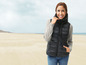 Een vrouw draagt een zwarte gewatteerde vest op een strand.