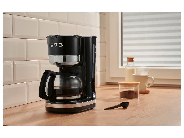 Zwart koffiezetapparaat met de tekst '1973' op een aanrecht met ontbijtbenodigdheden.