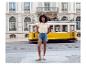 Vrouw in geborduurd T-shirt en denim shorts voor een rijdende gele tram.