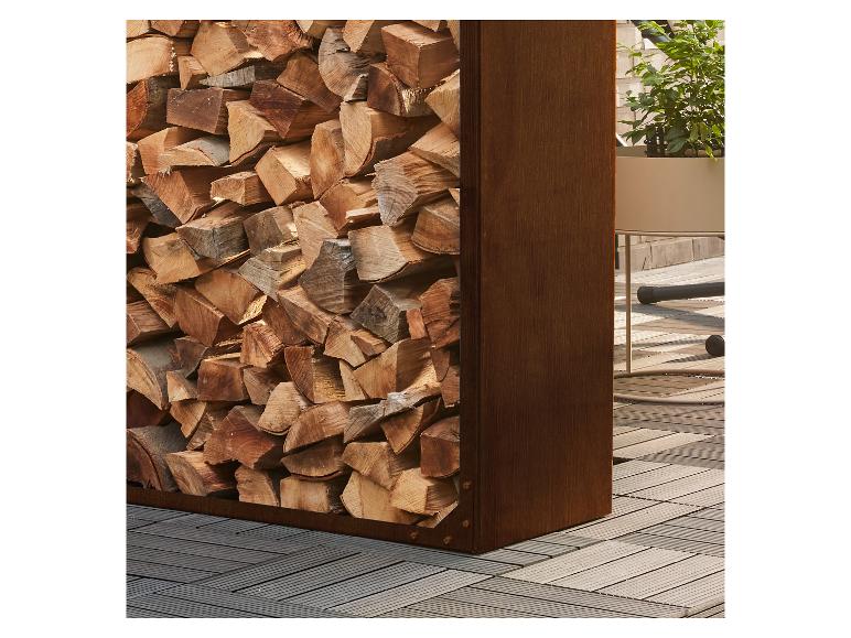 Stapel brandhout in metalen rek naast potplant op houten vloer.