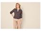 Vrouw in bruin gebreid vest en beige broek, poserend met hand in de zij.