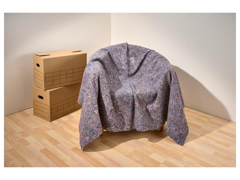 Fauteuil bedekt met verhuisdeken en stapel kartonnen dozen in een kamerhoek.