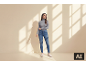 Vrouw in een grijze coltrui en blauwe jeans in een zonnige kamer.