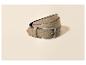 Een beige suède riem met een zilveren gesp, opgerold op een lichte achtergrond.