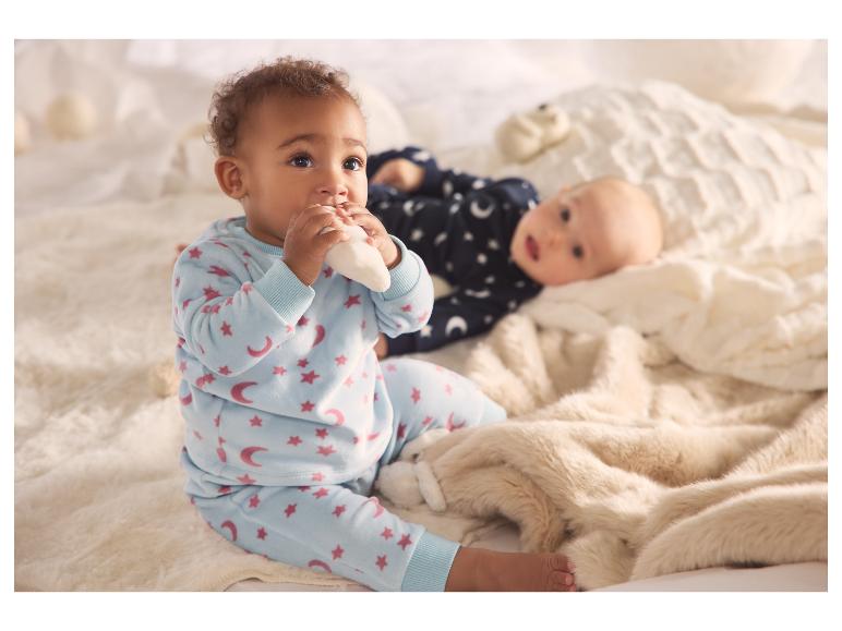 Twee baby's in zachte pyjama's, de een zittend en de ander liggend op een pluizige deken.