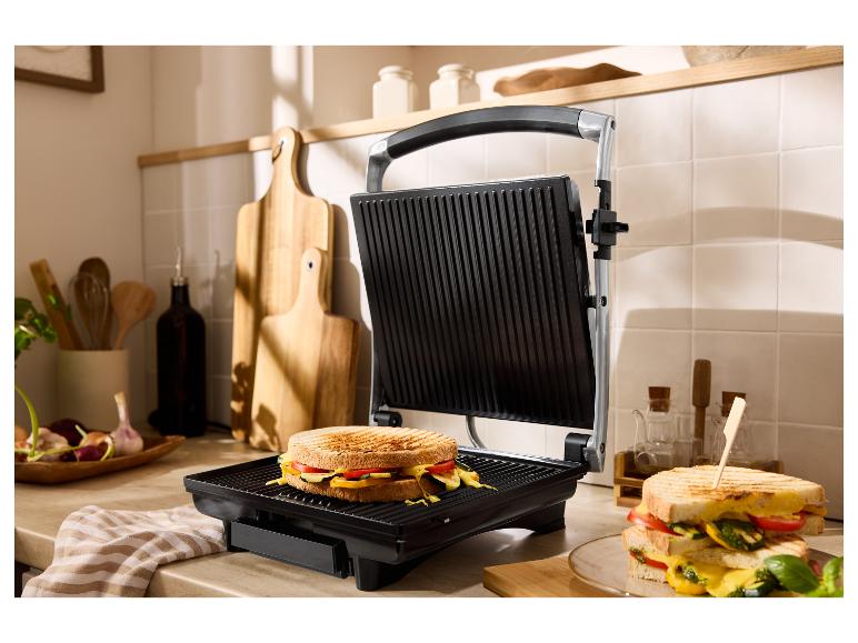 Een open grill met een gegrilde sandwich en een andere sandwich op een bord.