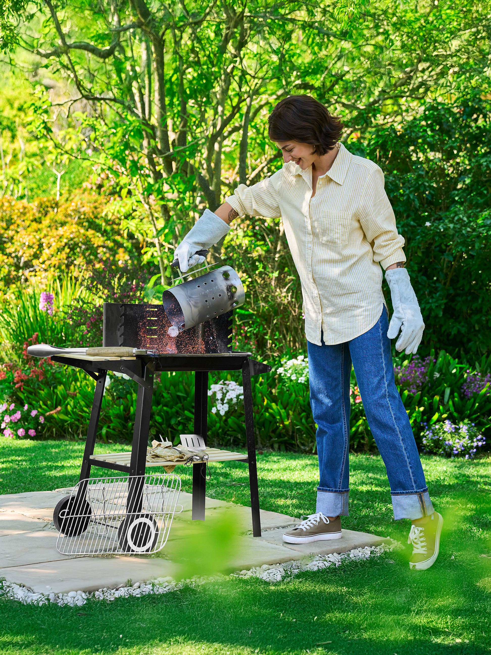 Vrouw giet kolen uit een brikettenstarter in een buitenbarbecue.