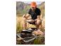 Man eet maaltijd bereid op draagbare grill en campingpan met bergen op de achtergrond.