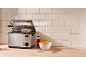 Friteuse met kippenvleugels en friet, saus en een kom friet op een houten tafel.