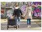 Familie met kind in kinderwagen wandelt hand in hand langs een graffitimuur.