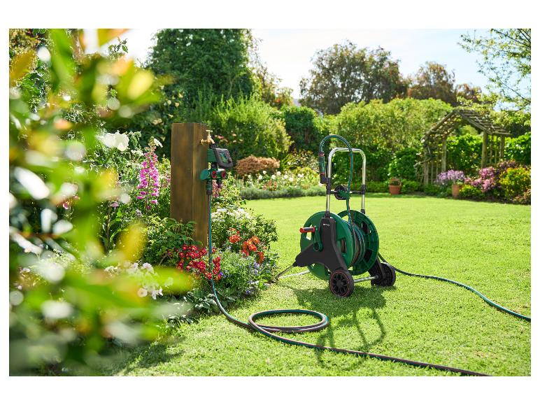 Tuinslang op een kar en een besproeiingstimer bij een houten paal in de tuin.