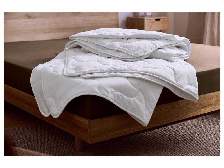 Wit gewatteerd dekbed op een bruin bed met een houten frame.