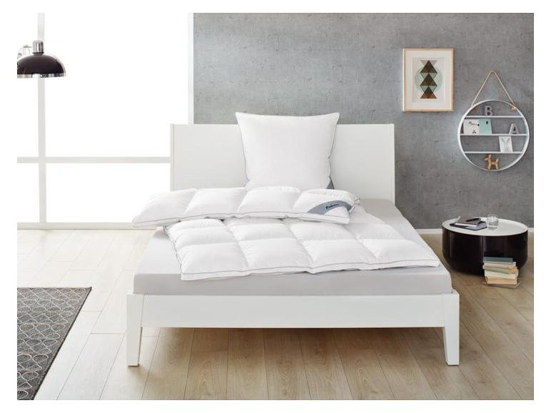Wit bed met wit dekbed en kussens, ronde nachtkast en wandplank.