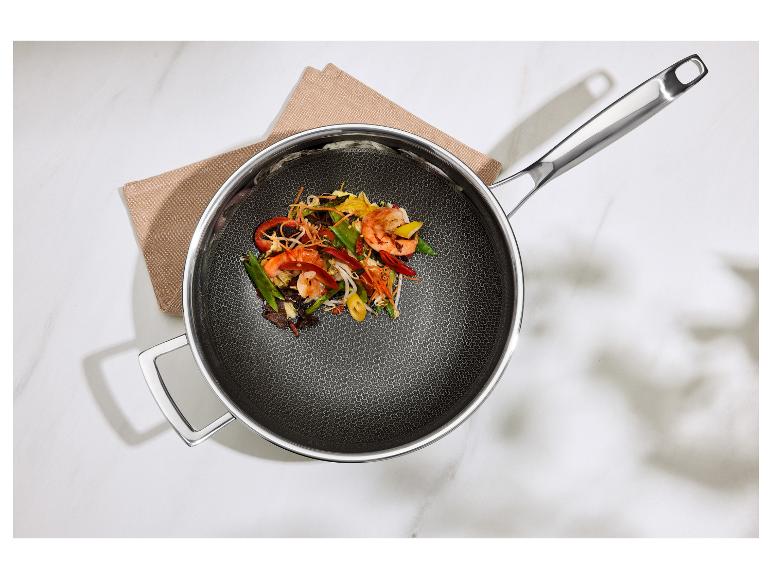 Koekenpan met metalen handvatten en roerbakgerecht met garnalen en groenten.