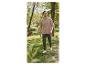 Man in beige t-shirt en groene broek loopt in park, hond op de achtergrond.