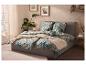 Bed met tropisch beddengoed, beige deken en planten in een lichte slaapkamer.