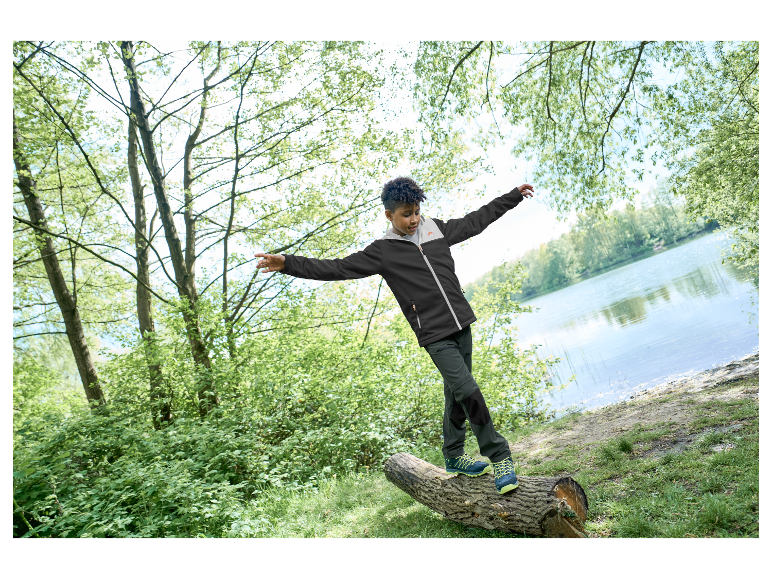 Kind in Jack Wolfskin jas en broek loopt over een boomstam.