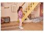 Meisje in paarse jas en roze legging staat in een kinderkamer met een trap.