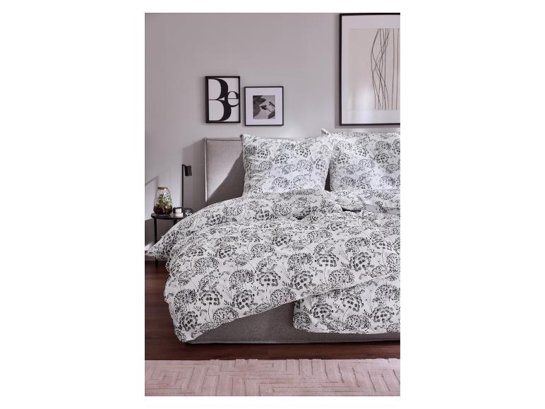Bed met wit dekbed met zwarte bloemenprint, kussens en grijs hoofdbord.