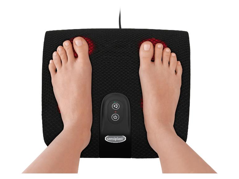 Voeten op een zwart elektrisch voetmassageapparaat met rode lampjes en bedieningspaneel.