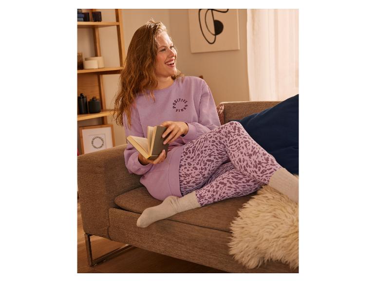 Een vrouw in een roze trui en leggings met dierenprint leest een boek op de bank.