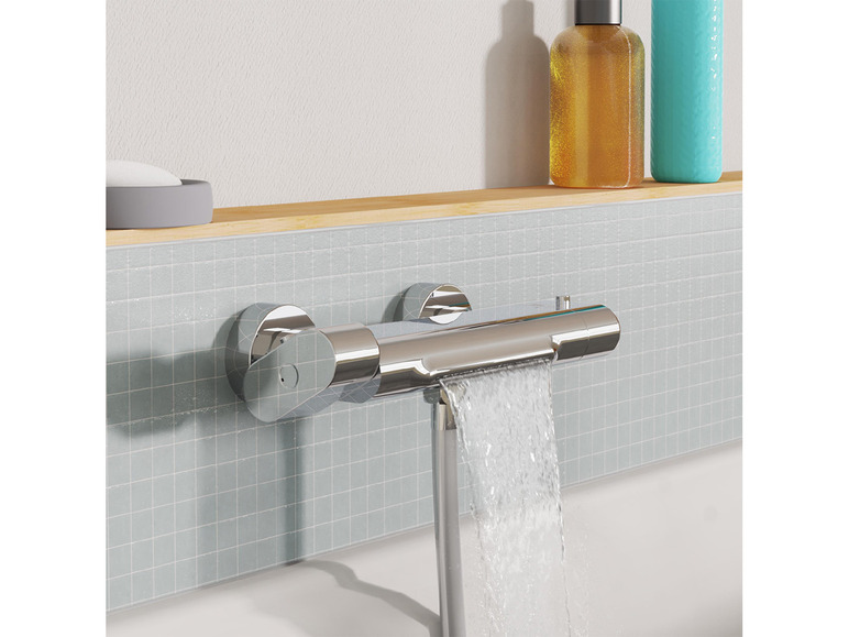 Een chromen badkraan met een watervalmondstuk op een grijze tegelwand.