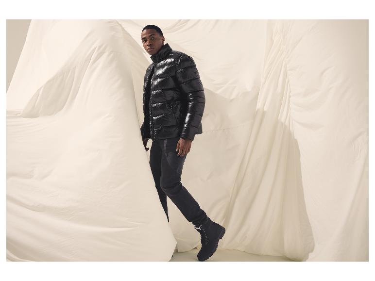 Man in glanzend zwart pufferjack en donkere jeans voor witte stof.