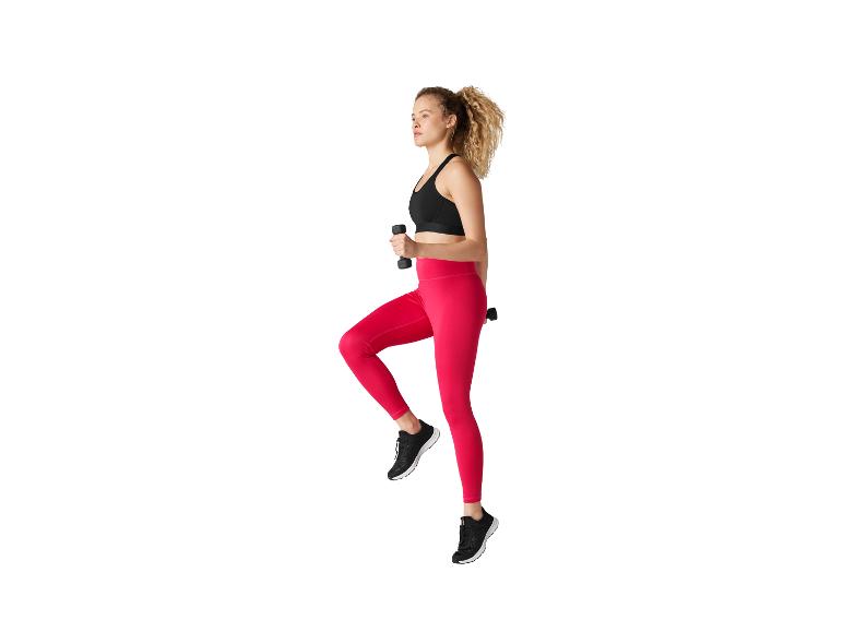 Vrouw in roze legging en zwarte sportbeha die oefent met dumbbells
