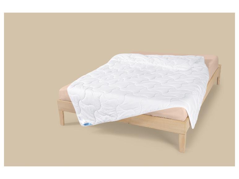 Wit gewatteerd dekbed op een houten bed met beige lakens.