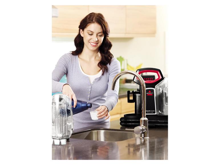 Vrouw bereidt een Bissell MultiClean Spot & Stain reiniger voor door oplossing aan water toe te voegen.