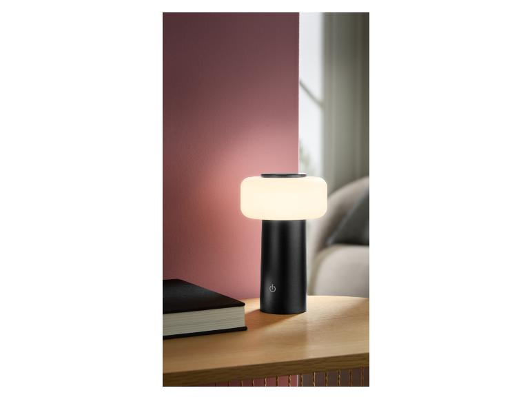 Zwarte draagbare tafellamp met wit licht op een houten nachtkastje naast een boek.