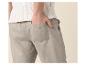 Man in een witte gebreide top en lichtgrijze linnen broek met hand in zak.