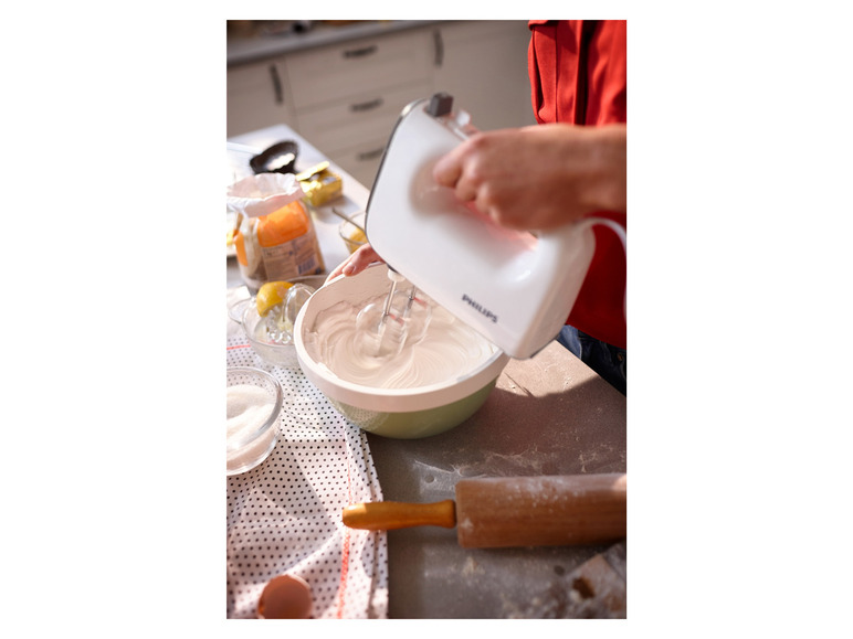 Een witte Philips handmixer klopt slagroom in een kom.