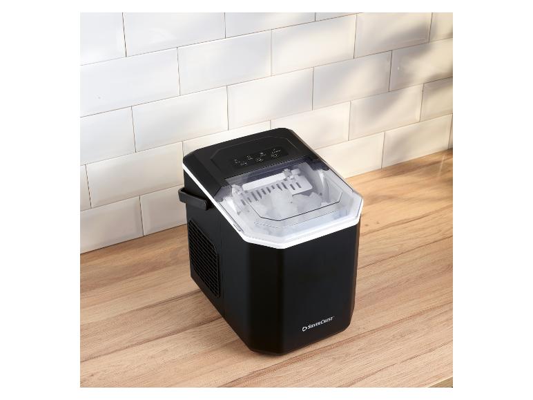 Zwarte ijsmachine met transparant deksel, vol ijsblokjes, op een houten aanrecht.