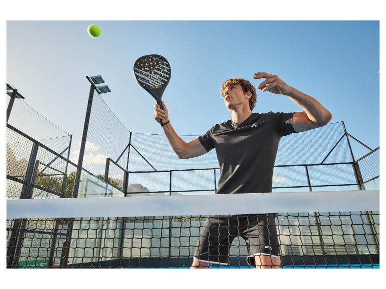 Man in zwarte sportkleding speelt padel met racket en bal.