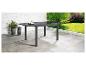 Grijze metalen en glazen tuintafel op een terras met planten en tuin op de achtergrond.