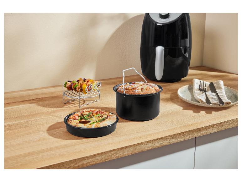 Airfryer met accessoires: spiesjes, bakvorm en pizzapan op een aanrecht.