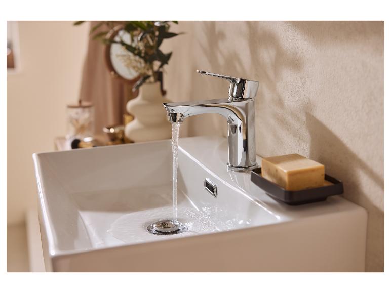 Chromen kraan met stromend water in een witte wastafel, met zeep ernaast.