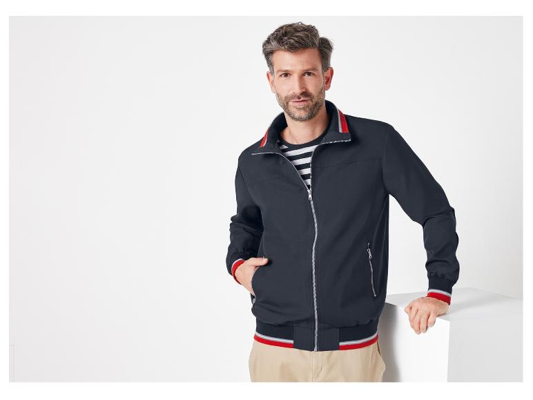 Een man draagt ​​een donkerblauwe bomberjack met rode accenten.