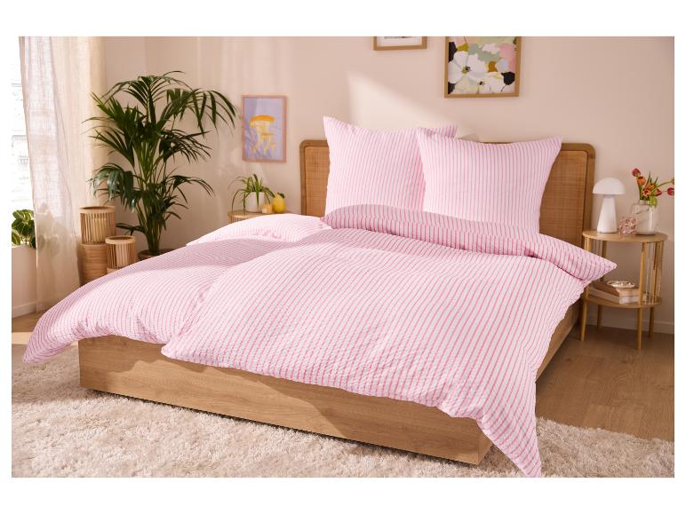 Roze gestreepte dekbedovertrekken op een bed, met planten en kunst aan de muur in de slaapkamer.
