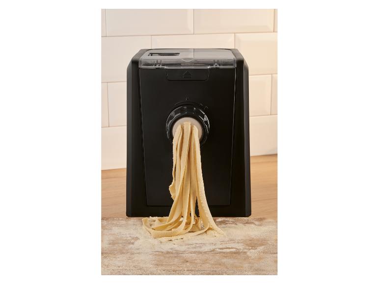 Automatische pastamaker die verse tagliatelle extrudeert op een bebloemde houten plank.