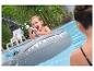 Jongen in opblaasbare haai schiet met waterpistool in zwembad.