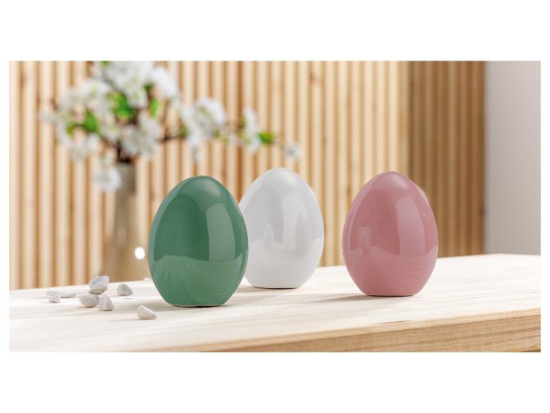 Drie eivormige keramische potten in groen, wit en roze op een houten tafel.