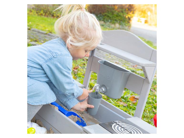 Kind speelt met een houten zand- en watertafel met kraan en emmer.