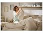 Vrouw in lichtgroene pyjama vouwt een beige deken in een lichte slaapkamer.