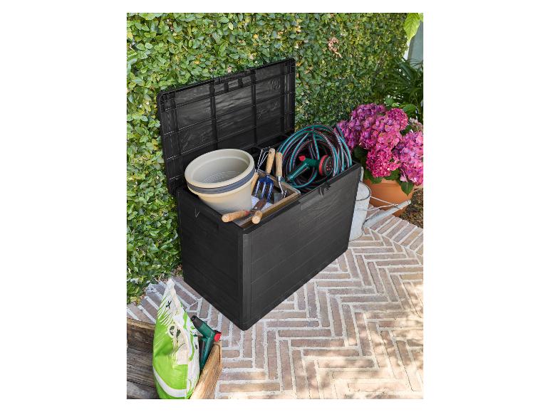 Zwarte tuinkist gevuld met tuingereedschap, een slang en een emmer, op een terras.
