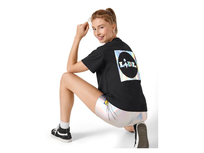 Vrouw in een zwart T-shirt met holografische print en zilveren shorts, gehurkt.