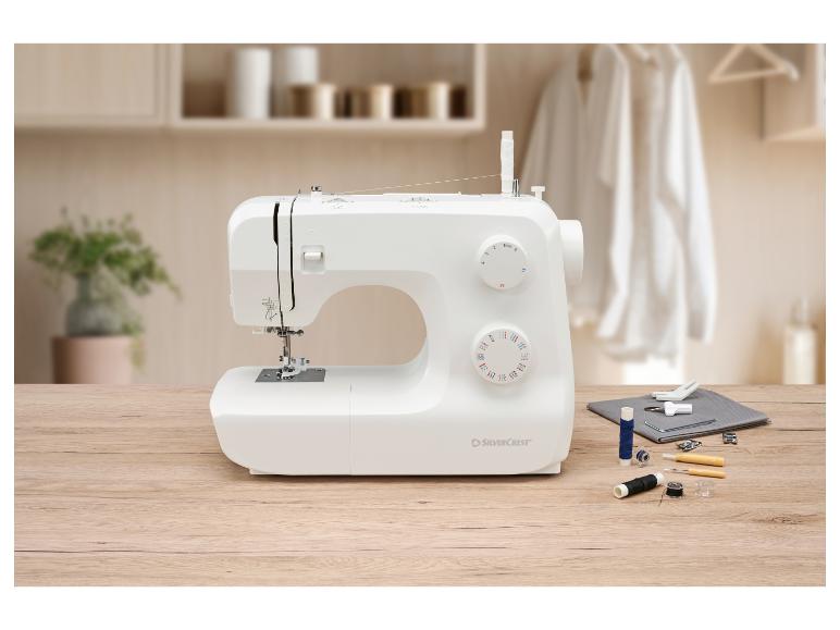 Witte naaimachine met naaibenodigdheden op een houten tafel in een lichte kamer.