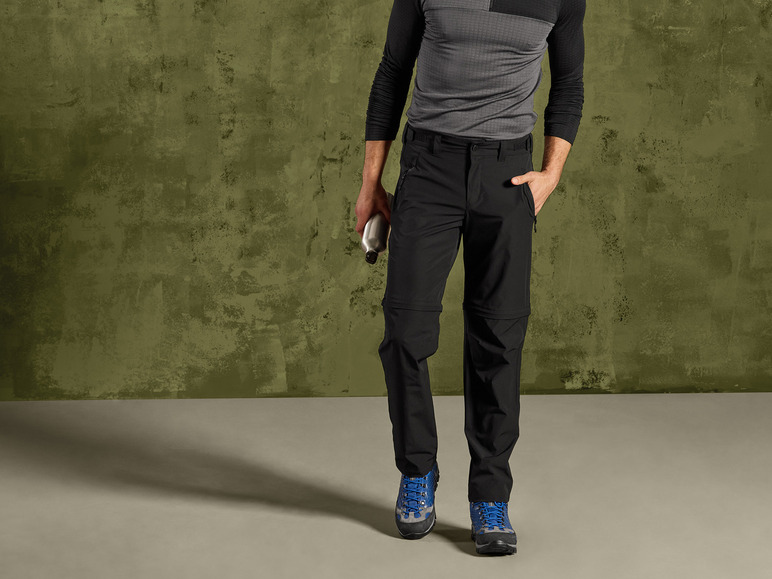 Een man draagt zwarte wandelbroeken en blauwe wandelschoenen.