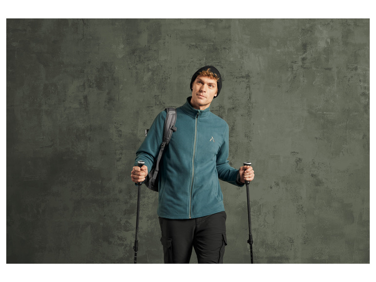 Een man met een groene fleecejas, rugzak en wandelstokken.